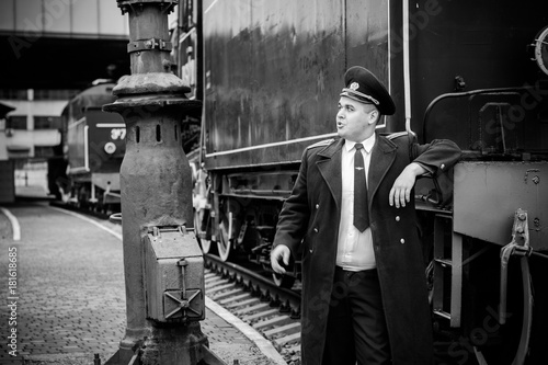 European or American train conductor is on his duty on a platform and other trains. Railway, steam trains, vintage trains .Train controller on the train, near a locomotive     © T.Den_Team