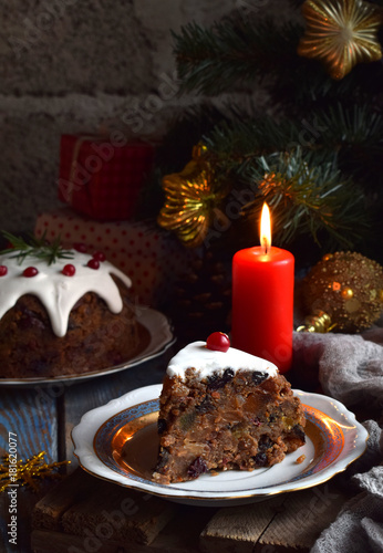 Traditional english Christmas steamed pudding with winter berries, dried fruits, nut in festive setting with Xmas tree and burning candle. Fruit cake