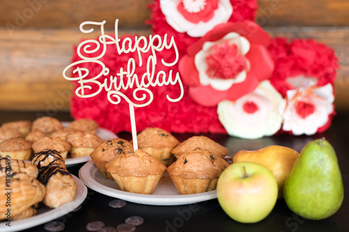Birthday cakes and muffins with wooden greeting sign on rustic background. Wooden sing with letters Happy Birthday and holiday sweets.