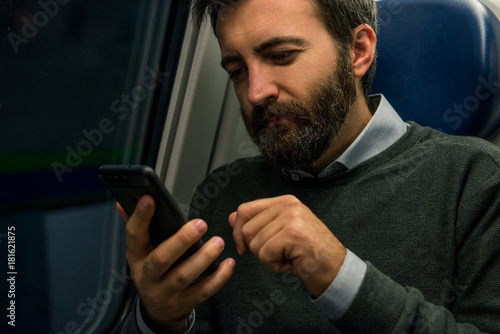Youn adul man commuter businessman seated on train look at smartphone during travel in the evening.