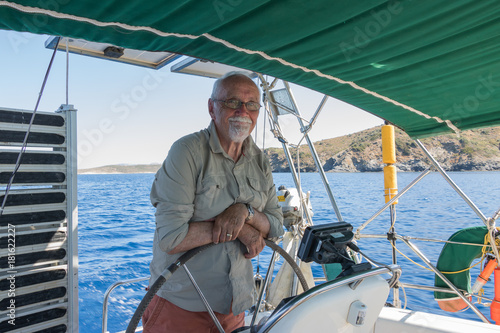 Old man holds a steering wheel of a boat and happy smiling. It`s a pleasure sailing in a blue sea. Fulfill your dreams to be a captain & yachtsman. Concept: active elderly people. 