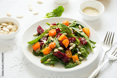 Fresh autumn salad with marinated pumpkin and beetroot  spinach leaves olive oil  sesame and pumpkin seeds on white table cloth. Space for copy
