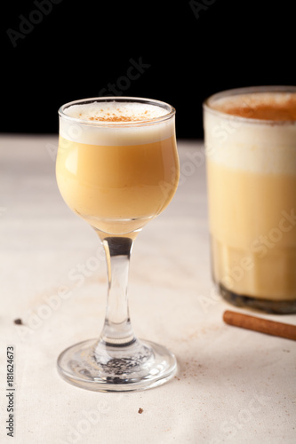 Two glasses with christmas eggnog drink decorated with cinnamon on dark background. Vertical composition.