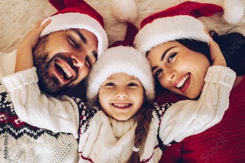 Christmas family! Happy mom,dad and little daughter on Santa Claus hats lying down. Enjoyng love hugs, holidays people concept