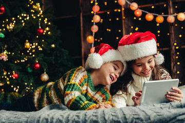 Christmas holidays at home. Happy children using tablet, playing online, having fun.