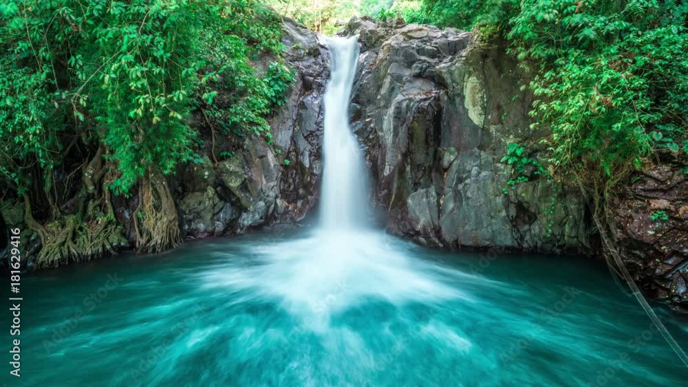 Timelapse Tropical waterfall flows through dense jungle forest and falls into wild pond in Bali, Indonesia Timelapse Tropical waterfall flows through dense jungle forest and falls into wild pond in Bali, Indonesia