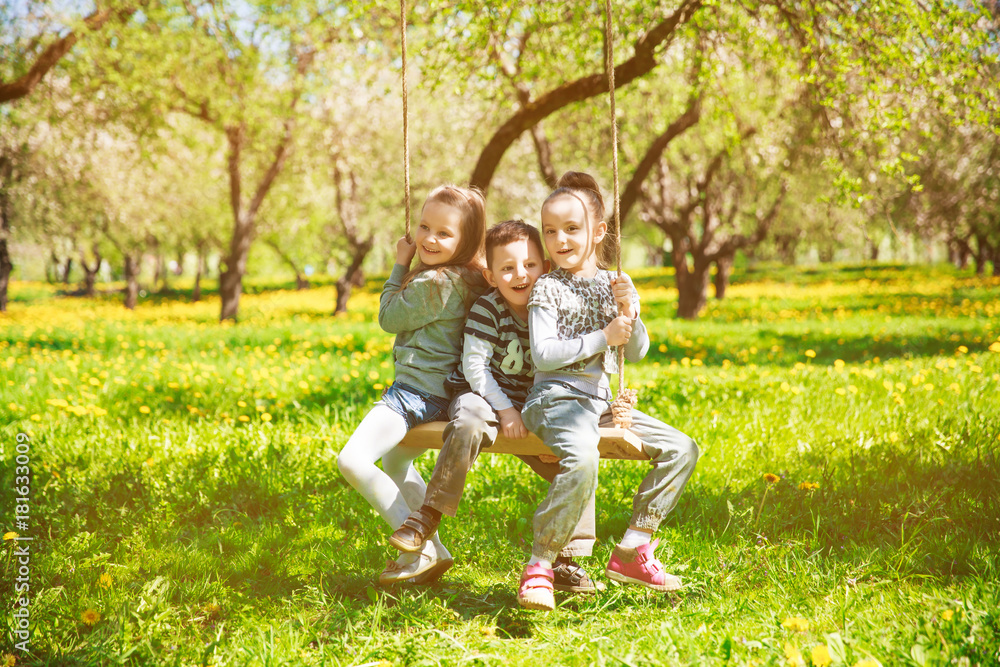 Three small children ride on the swings in the Park