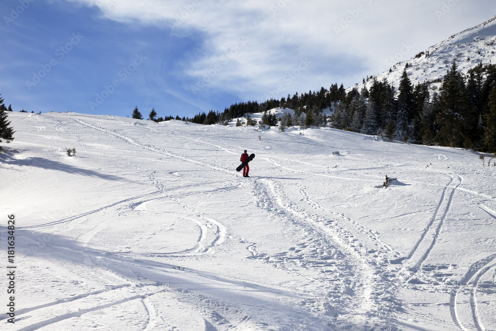 Snowboarder on snow off-piste slope with snowboard in hands at sun winter morning