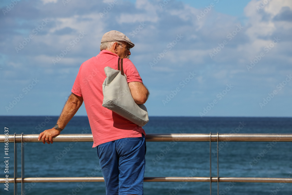 A modern old man is looking on a blue sea & sky. It`s a beautiful skyline over there. Concept: travels & active elderly people.