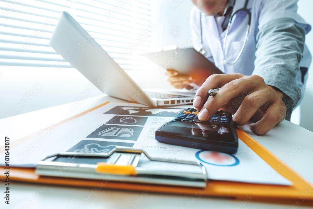 Fototapeta premium Healthcare costs and fees concept.Hand of smart doctor used a calculator and smartphone for medical costs at modern hospital in sun light