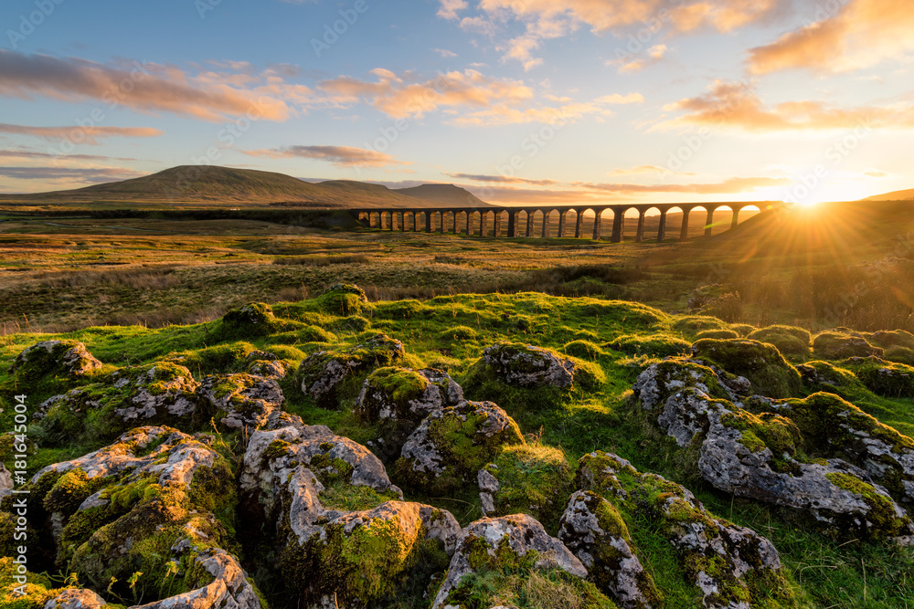 Gorgeous golden light as the sun sets behind the Ribblehead Viaduct with rocks in foreground. - obrazy, fototapety, plakaty 