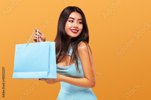 Shopping Festival . Happy asian woman at shopping holding bag and phone isolated on blue background on Black Friday holiday. Copy space for sale ads.