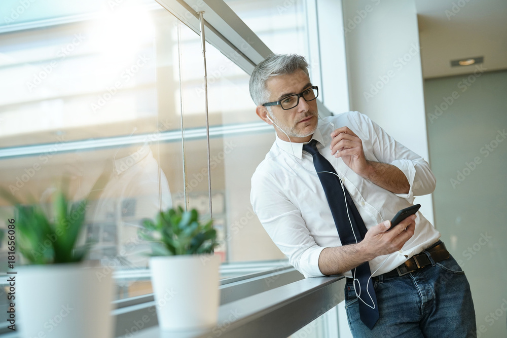 Businessman talking on phone in office, standing by window Businessman talking on phone in office, standing by window
