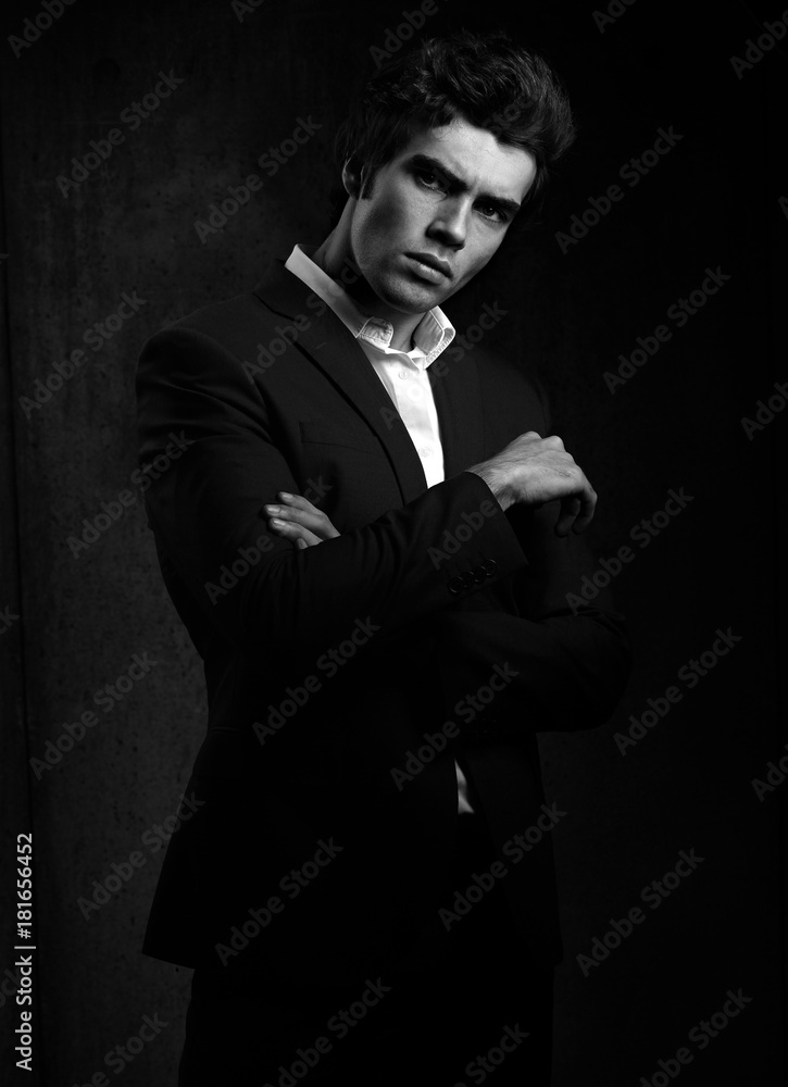 Handsome male model posing in fashion suit and white style shirt looking on dark shadow background. Black and white portrait Handsome male model posing in fashion suit and white style shirt looking on dark shadow background. Black and white portrait