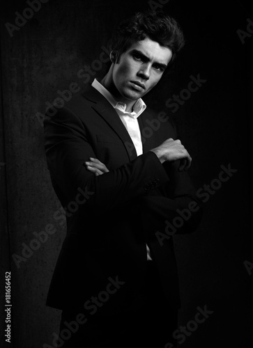 Handsome male model posing in fashion suit and white style shirt looking on dark shadow background. Black and white portrait © nastia1983