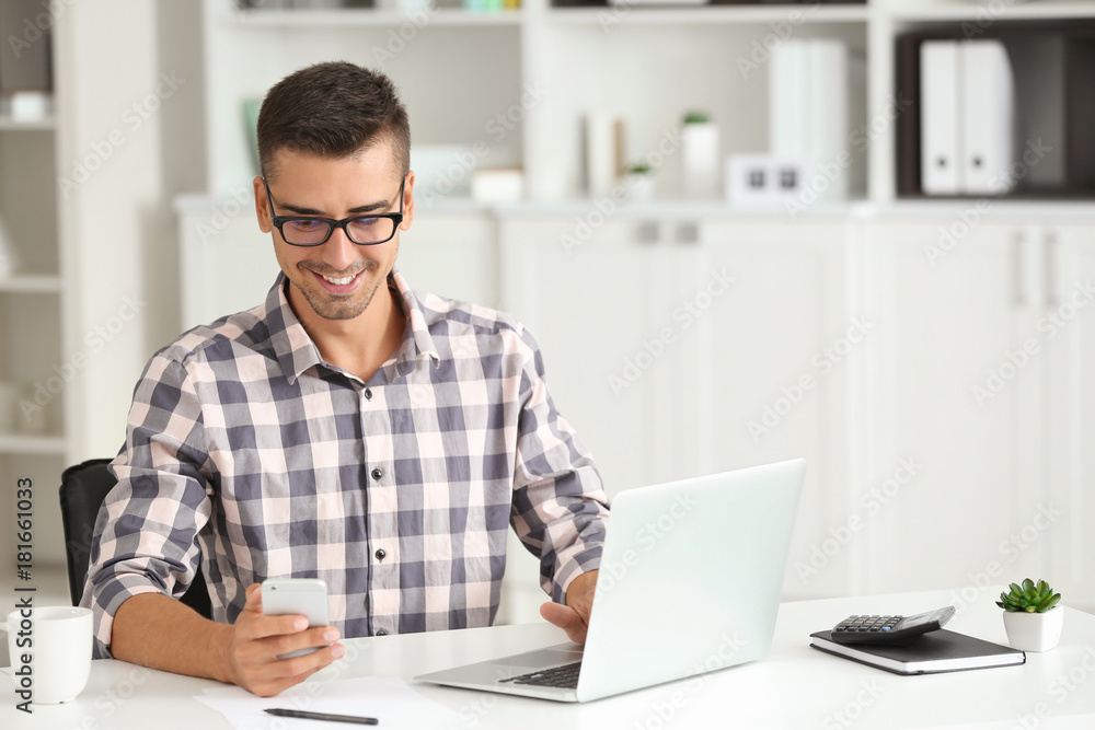Attractive man with laptop and smartphone in office Attractive man with laptop and smartphone in office