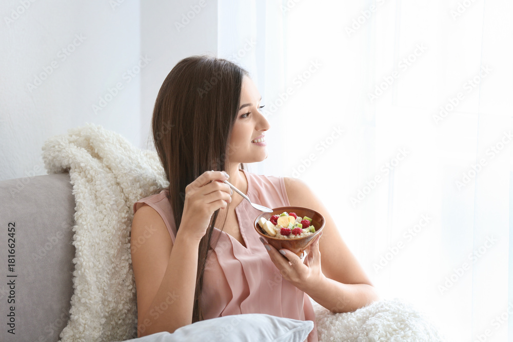 Young woman eating oatmeal on sofa at home Young woman eating oatmeal on sofa at home
