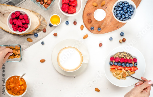 Good morning - healthy breakfast background with oatmeal coffee, berries, egg, nuts. Coffee, hands, hold, cup. White wooden food background, top view © conssuella