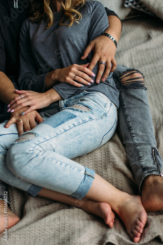 Cropped view of youngcouple embracing and relaxing on bed at home. Vintage casual look. Torn blue jeans. Winter time