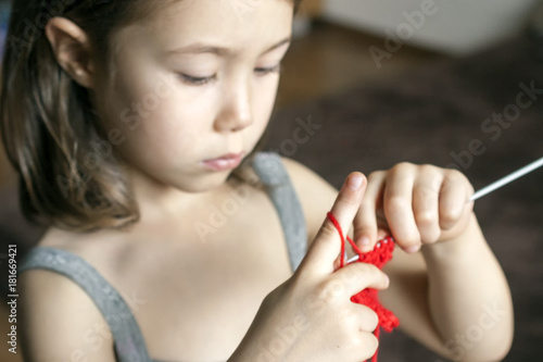 The little girl concentrated on knits on the needles of red wool yarn
