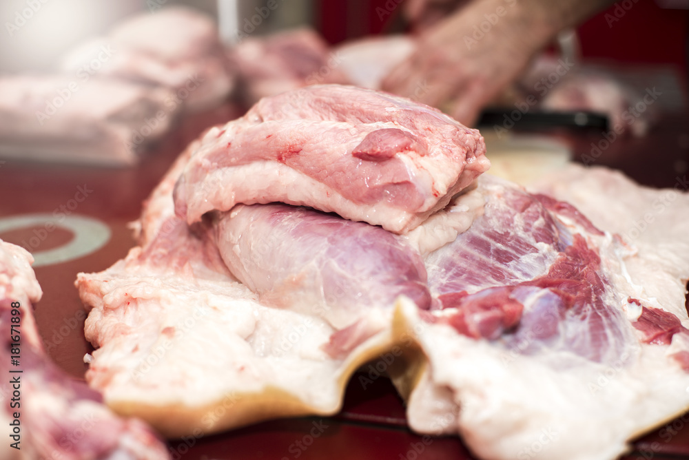 Pieces of pork meat, a man cutting meat in the background, working process