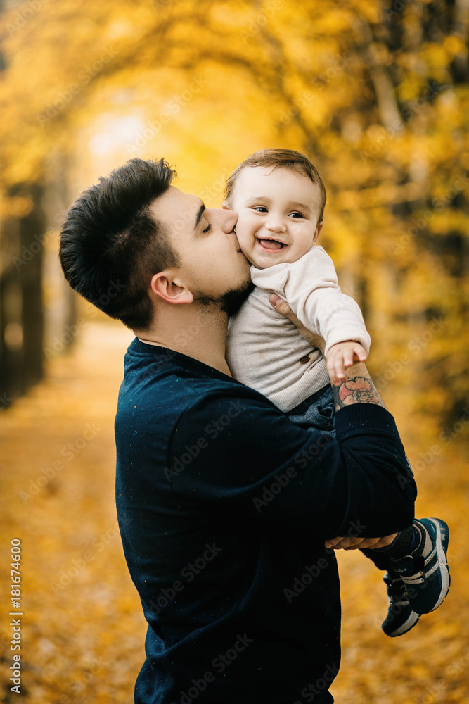Father and Son walking. Baby taking first steps with father help in autumn garden in the city Father and Son walking. Baby taking first steps with father help in autumn garden in the city