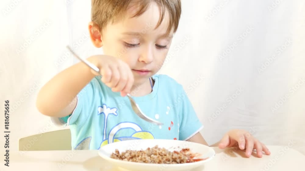 The child eats buckwheat porridge with meat, sitting at the table. The child eats buckwheat porridge with meat, sitting at the table.
