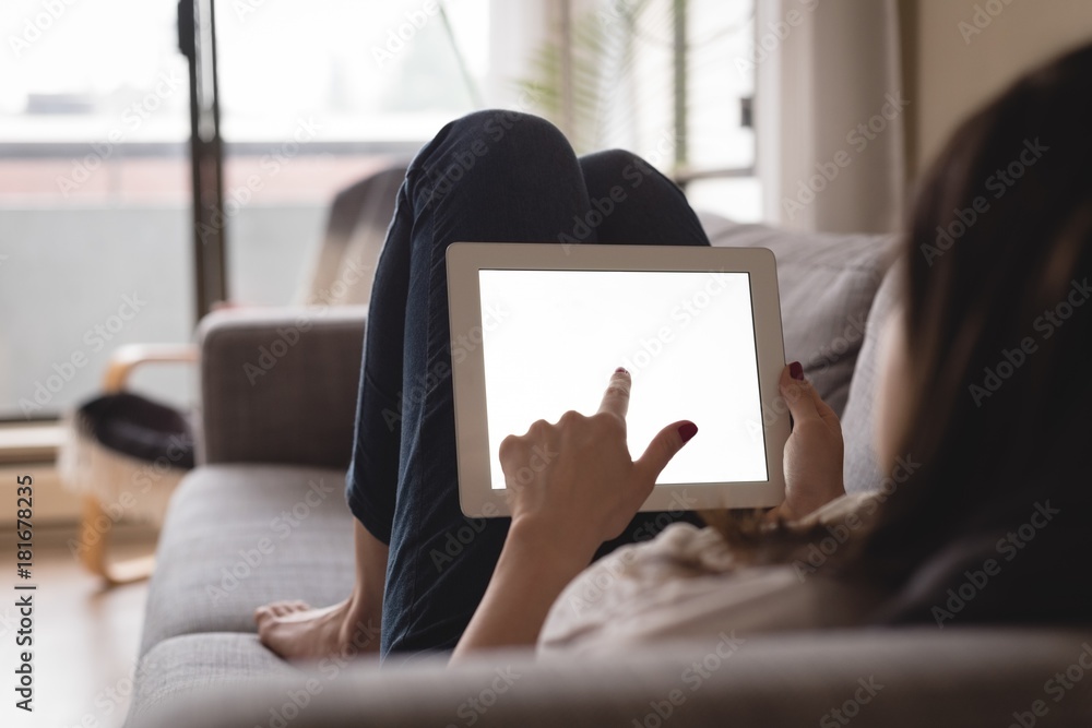 Young woman using digital tablet while lying on sofa Young woman using digital tablet while lying on sofa