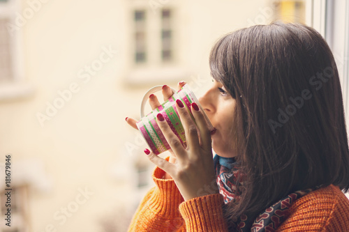 Young woman drinking coffee by the window in warm home