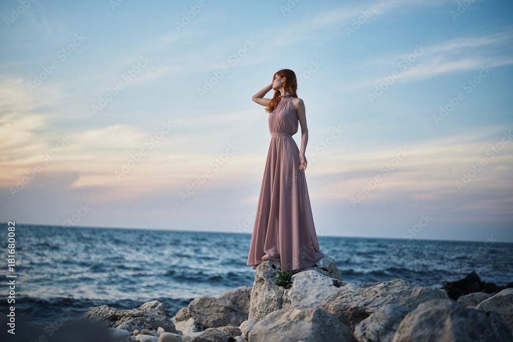 Beautiful young woman in a long dress is standing on the sea