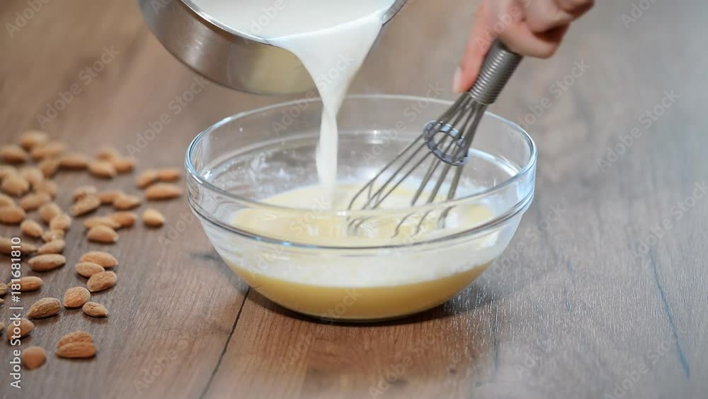 A woman in the kitchen to cook the custard. Milk pouring in bowl A woman in the kitchen to cook the custard. Milk pouring in bowl