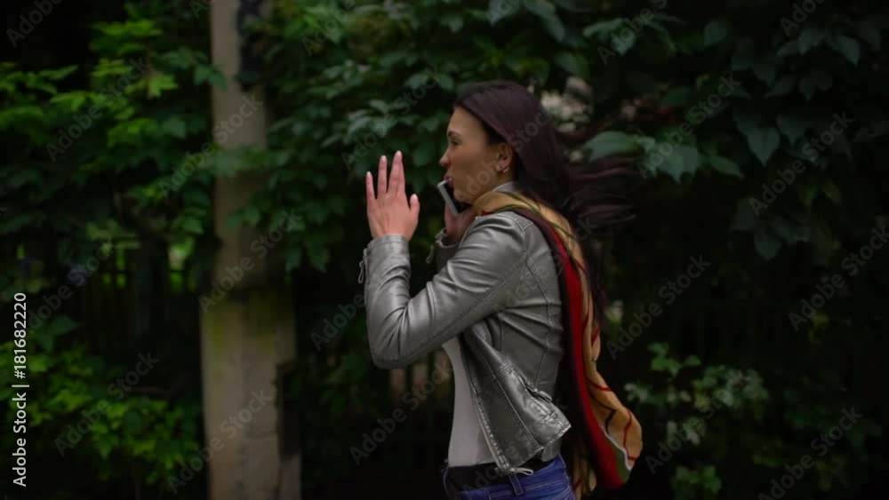 Young woman is talking on the phone on the run, she is in a hurry. outdoors in summer. slow-motion Young woman is talking on the phone on the run, she is in a hurry. outdoors in summer. slow-motion