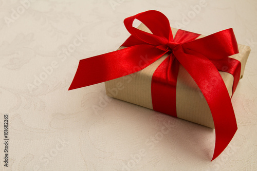 Gift box with the red ribbon on the beige tablecloth