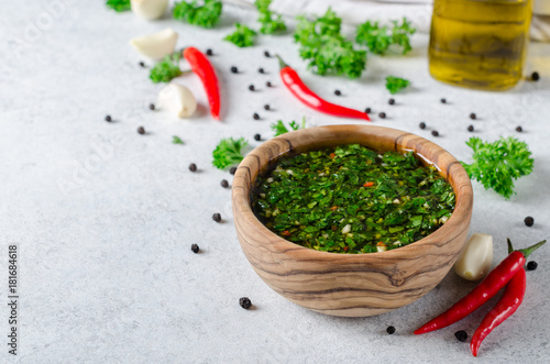Traditional argentinian chimichurri sauce made of parsley, cilantro, garlic and chili pepper in a wooden bowl. Selective focus, horizontal image photo