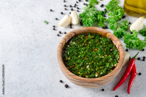 Traditional argentinian chimichurri sauce made of parsley, cilantro, garlic and chili pepper in a wooden bowl. Selective focus, horizontal image