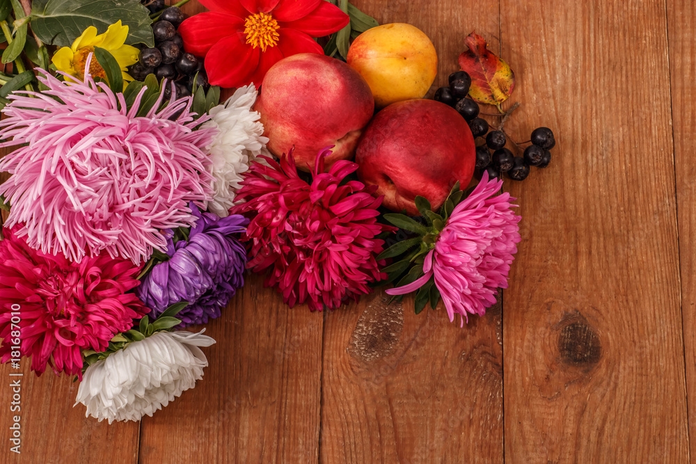 brown wooden background with bright autumn asters, red fruit and chokeberry