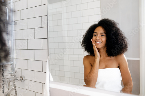 Young woman standing in front of a mirror, massaging her face with hand