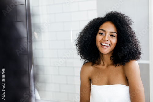 Portrait of a happy young woman standing in the bathroom while wrapped in a towel