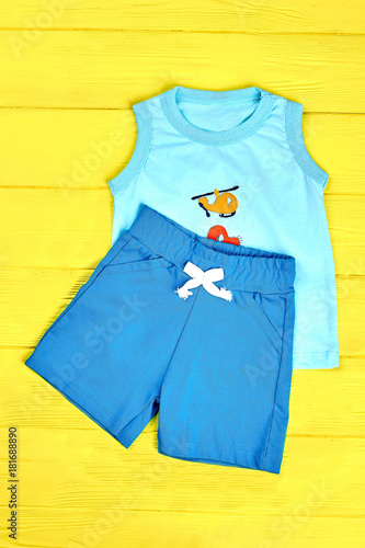 Baby boy cute cotton suit. Toddler boy blue shorts and sleeveless t-shirt on yellow wooden background. Kids high quality summer clothes on sale. © DenisProduction.com