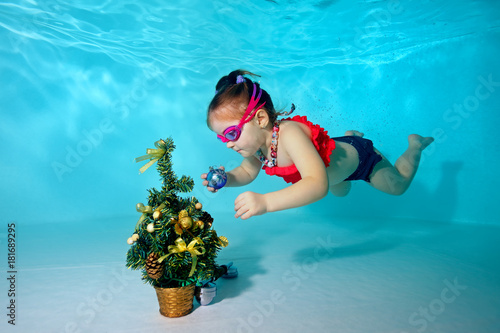 Child underwater in the pool decorates the Christmas tree with Christmas toys. Portrait. Shooting under water. Horizontal orientation