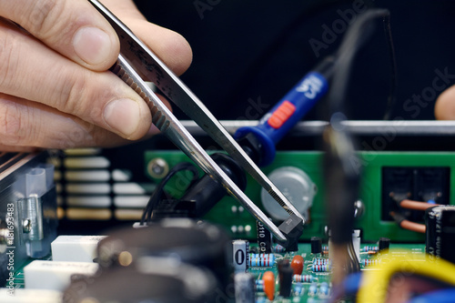 Repairman disassembling smartphone with tweezers. Unrecognizable man holding computer circuit in electronics repair service