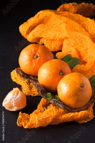 Fresh ripe mandarins with mint on wood bark bowl, orange textile on black background. Modern dark mood style. Vertical banner. Closeup photography