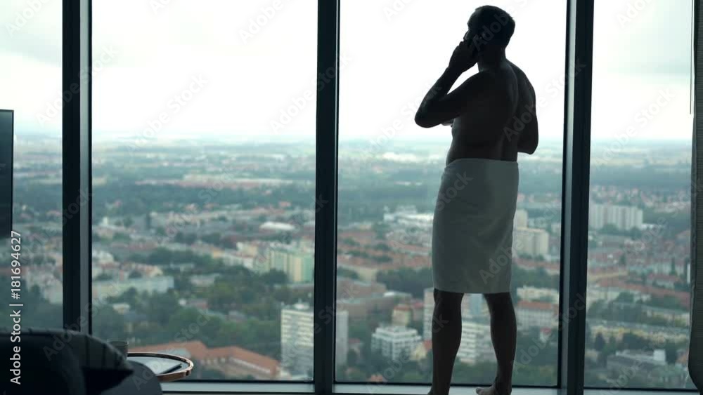 Man in towel talking on cellphone and drinking water by window
Man in towel talking on cellphone and drinking water by window