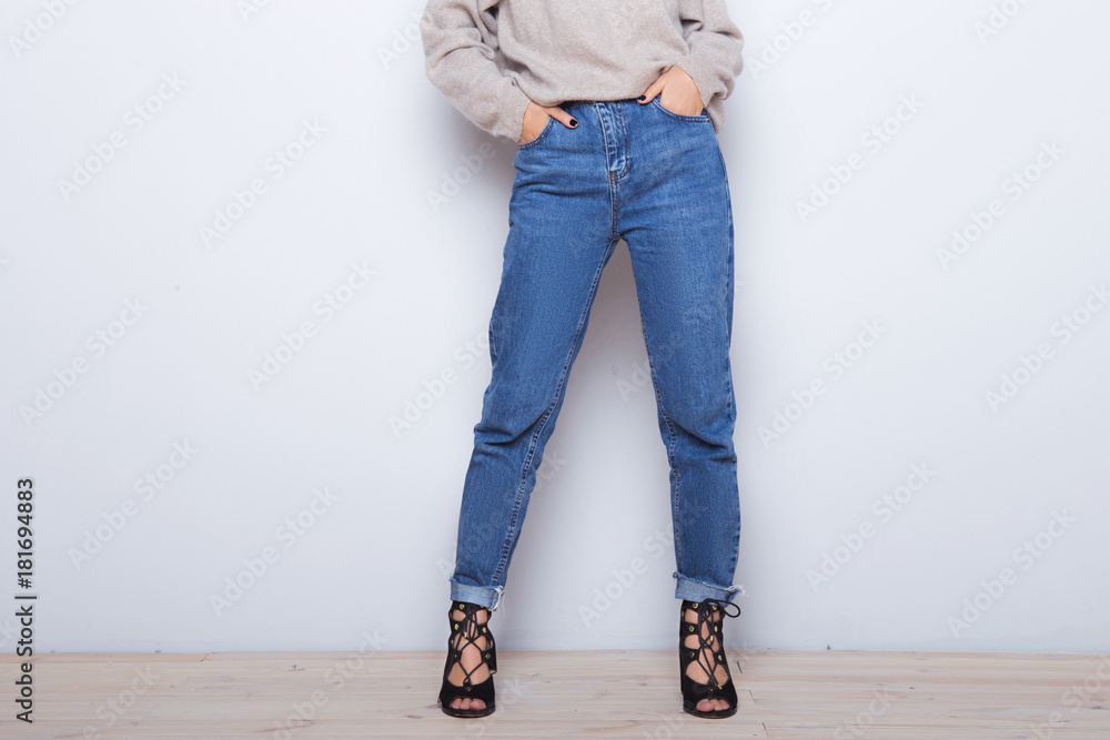 Fashion jeans on a girl. Thin legs of fashion girl. Shapely female legs in high heel shoes and jeans near a white wall Fashion jeans on a girl. Thin legs of fashion girl. Shapely female legs in high heel shoes and jeans near a white wall