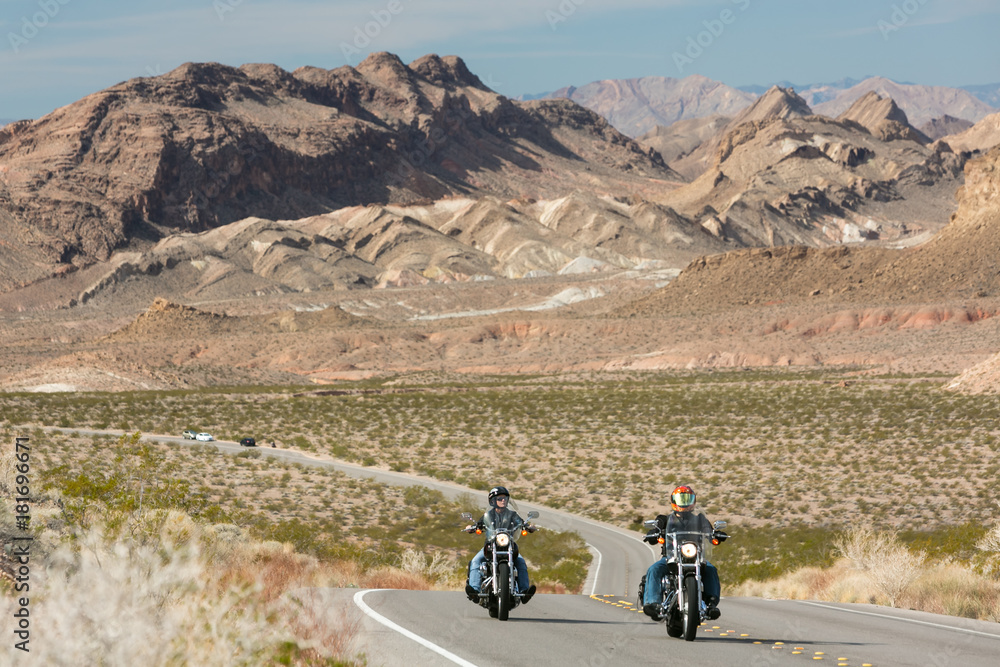 Two motorcycles travel along mountainous desert landscape Two motorcycles travel along mountainous desert landscape
