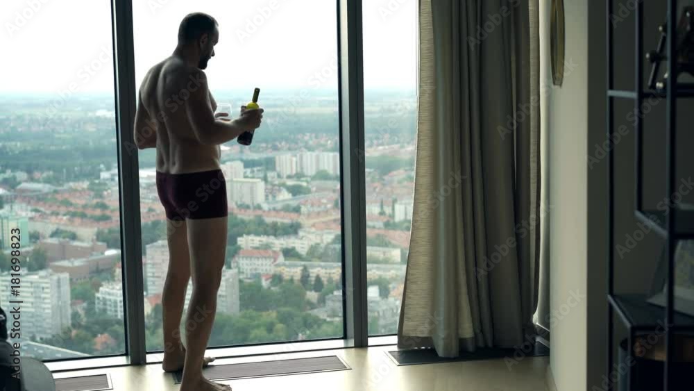 Man in underwear drinking wine and admire view from window at home
Man in underwear drinking wine and admire view from window at home