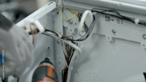 Unscrewing screws that are on the inner side of the broken washing machine. Repairman is helping with baterry power drill. photo