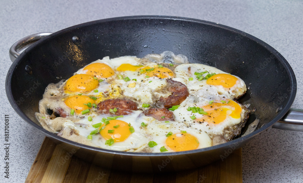 Fried eggs with sausage and chives on a deep black pan closeup Fried eggs with sausage and chives on a deep black pan closeup