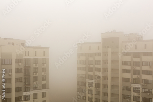Top part of highrise modern apartment building facade during heavy fog weather