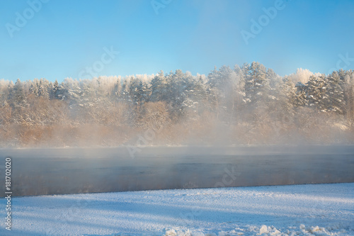 Morning steam fog above river. Winter landscape. Frosty day on the river. Part of the river is covered with ice. Swirl the water vapor. Harmonious colours. The texture is horizontal. Place for text. © pesenka77